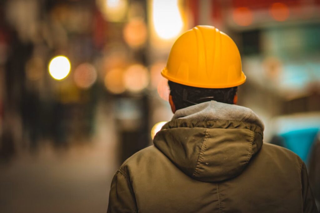 Man in yellow hard hat and hoodie with his back turned to camera