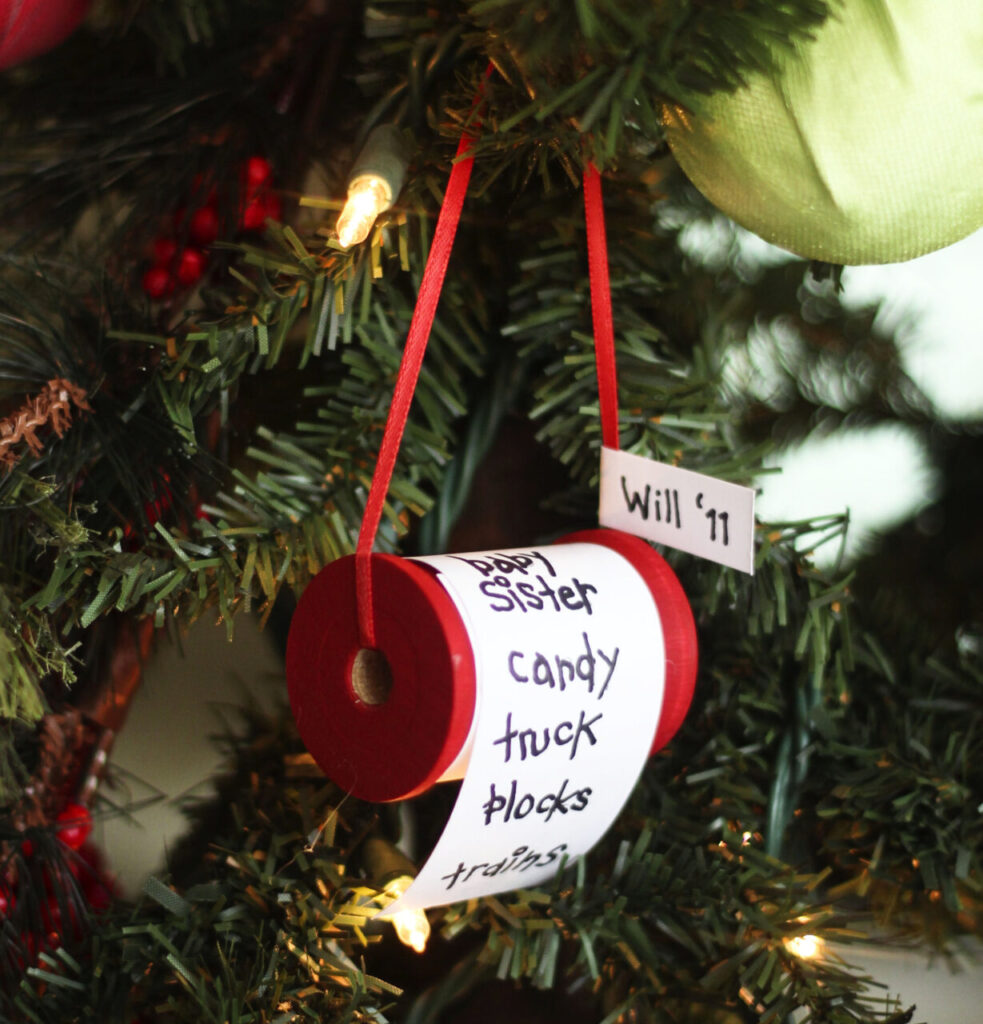 A rolled up Christmas wish list hangs on a fake tree covered in yellow-white lights.