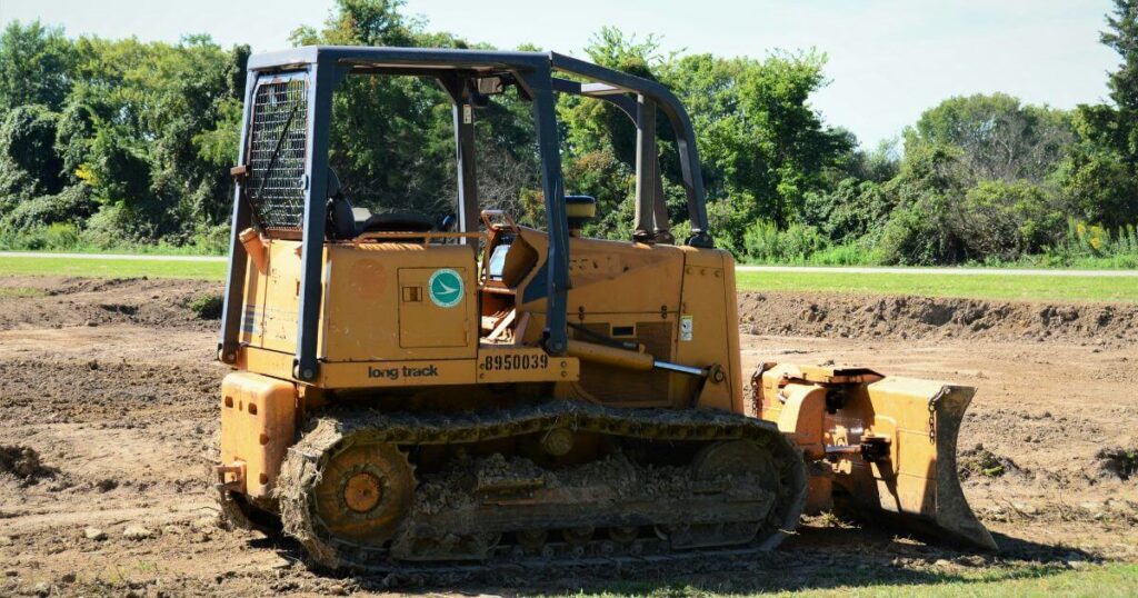 A compact grader maneuvering a worksite. The grader is tracked with a roll cage.