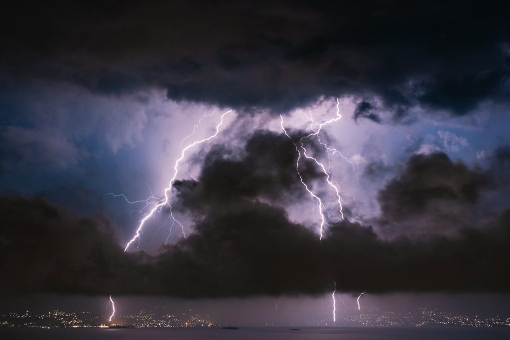 Lighting streaks fill a dark cloudy sky over a city at night.