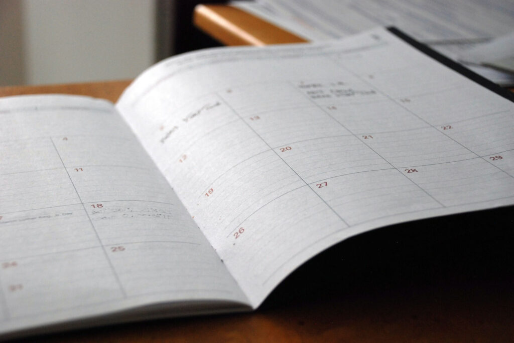 A monthly paper planner sits open to an unknown month, likely to help someone keep track of deadlines for independent contractor tax rates.