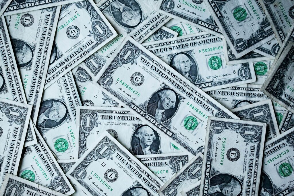 A pile of one-dollar bills sits spread out on a flat surface.