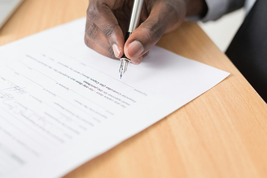 A man signs paperwork with a fountain pen on a light wood table.