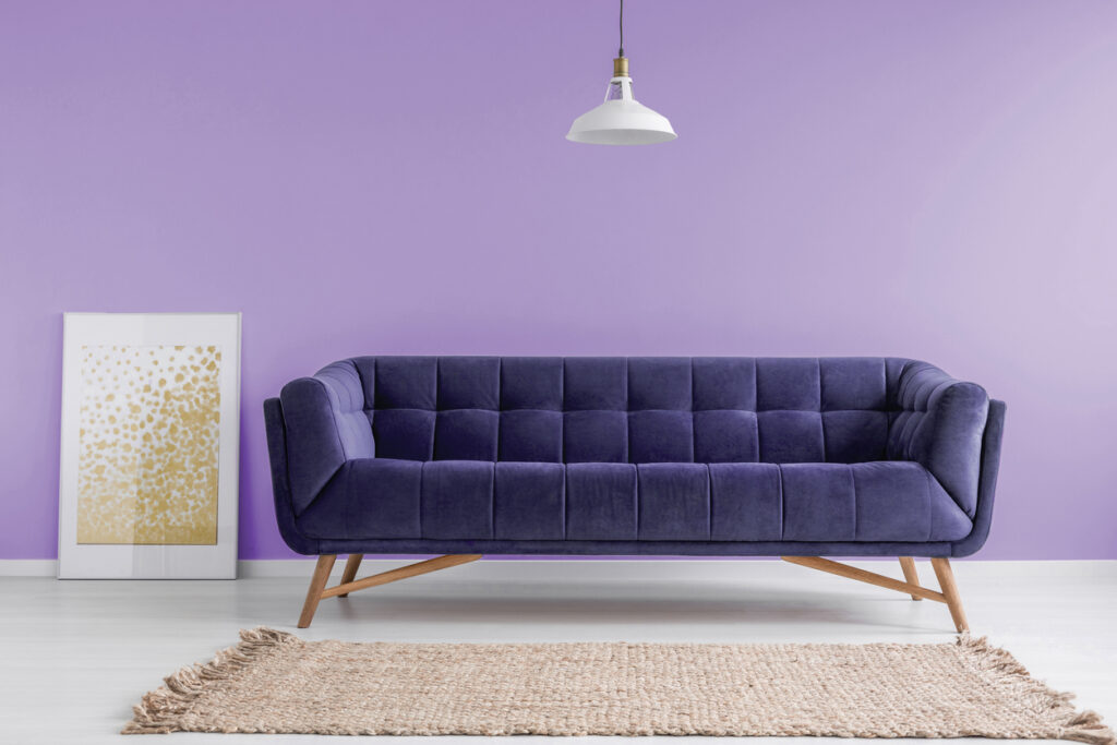 Purple, velvet sofa and a beige rug in a pastel lavender living room interior