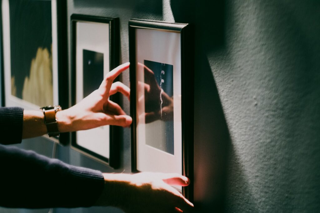 a woman hanging a black photo frame in line with others