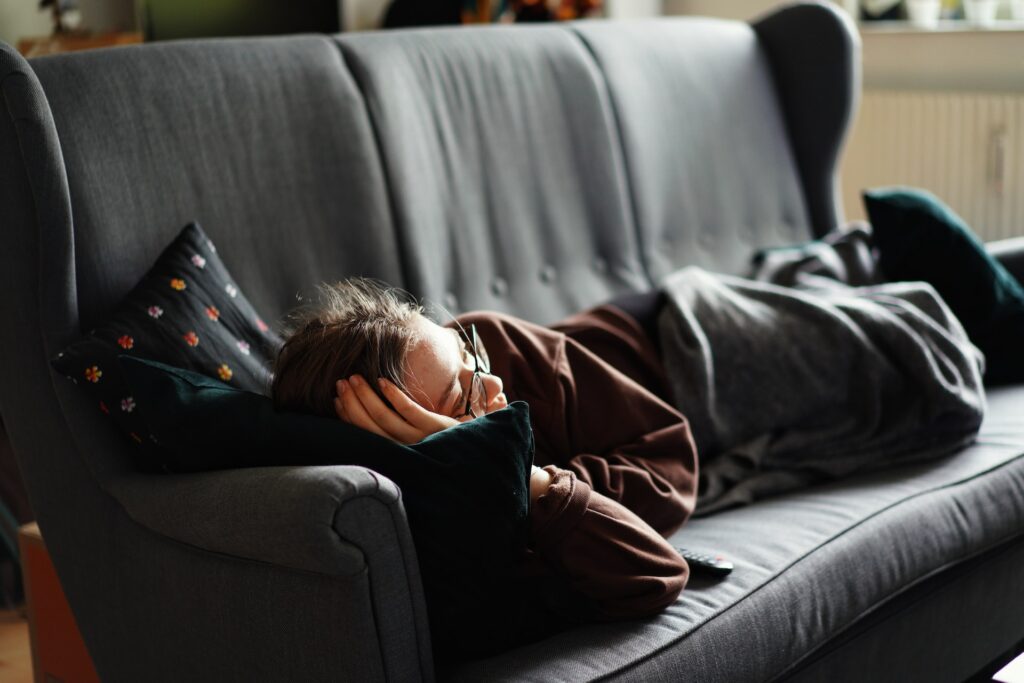 a woman in glasses laying on a grey couch