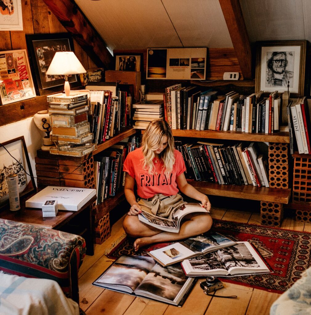a woman sitting on a wooden floor reading books in front of bookshelves