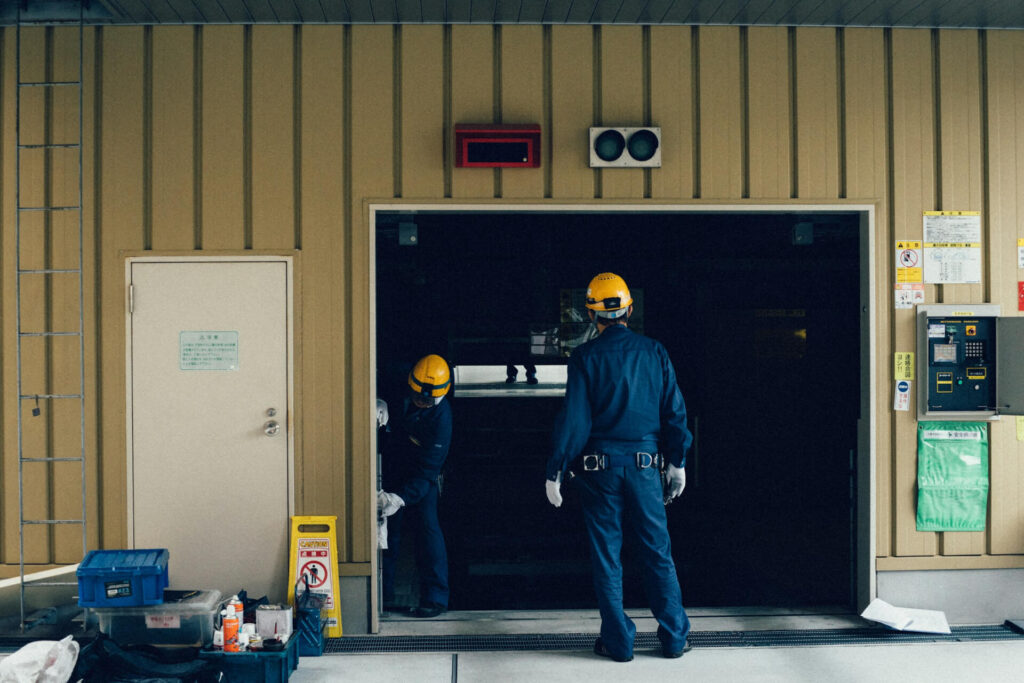 Two people in yellow construction hats working on a garage door