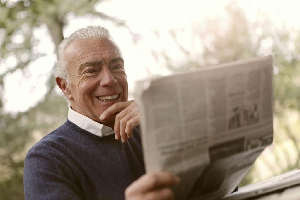 A smiling elderly man reading the newspaper.