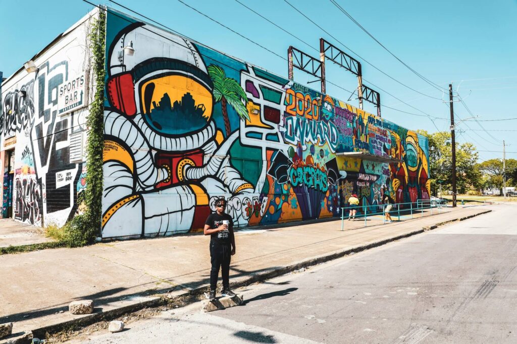 A young person standing in front of a sports bar building covered with graffiti in Houston.