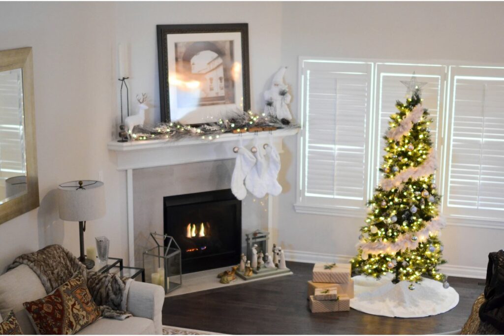 An artificial tree decorated with a string of lights and three socks hanging by the mantel of an electric fireplace.