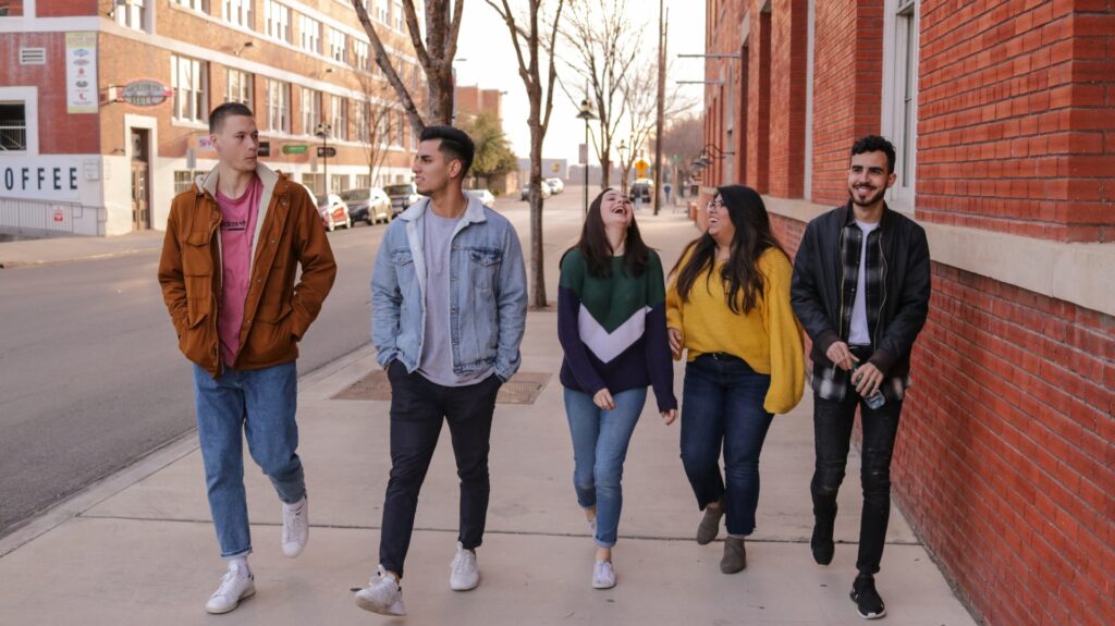 A group of five people walking down the street in a safe U.S. city. There are red brick buildings on both sides of the street and trees without leaves line the sidewalk.