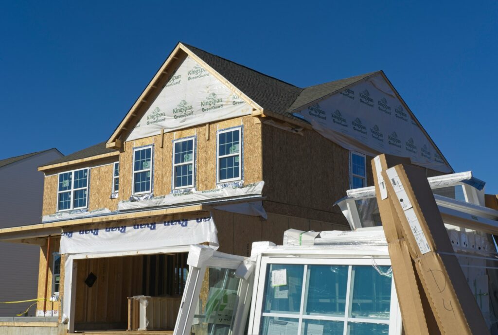 A two-story residential house is mid-construction under a blue sky.