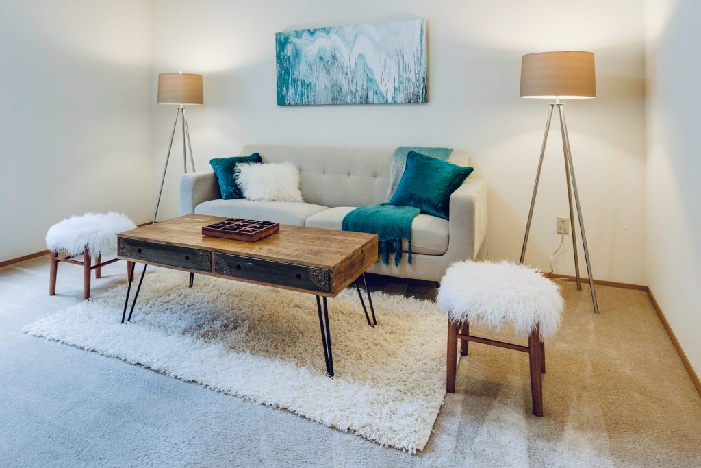 A bright living room with a white plush carpet and plush stools as a way to create a space for self-care at home