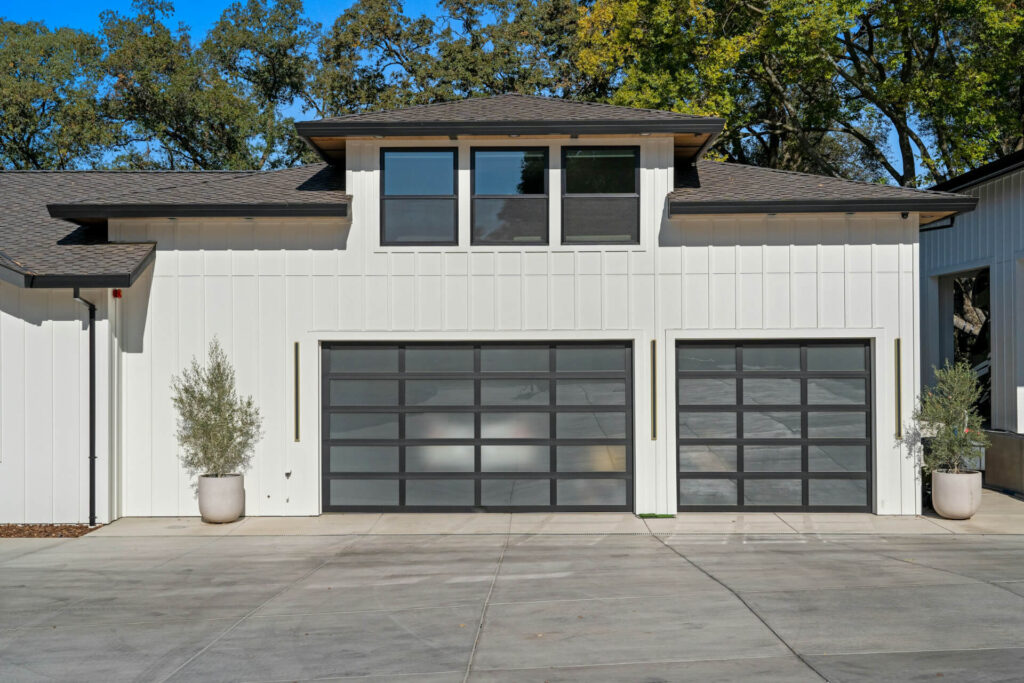 A white house with two semi-transparent garage doors, one rectangular and one square