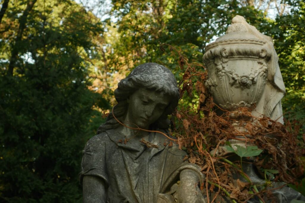 A weathered statue of a person with dried vegetation