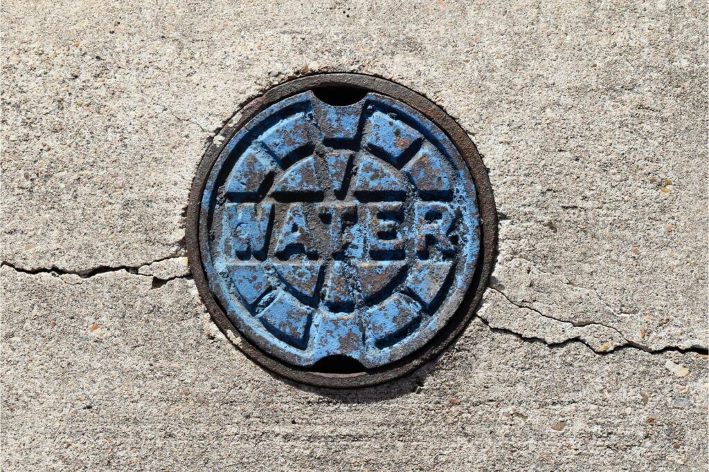 A rusty manhole cover labeled water with peeling paint