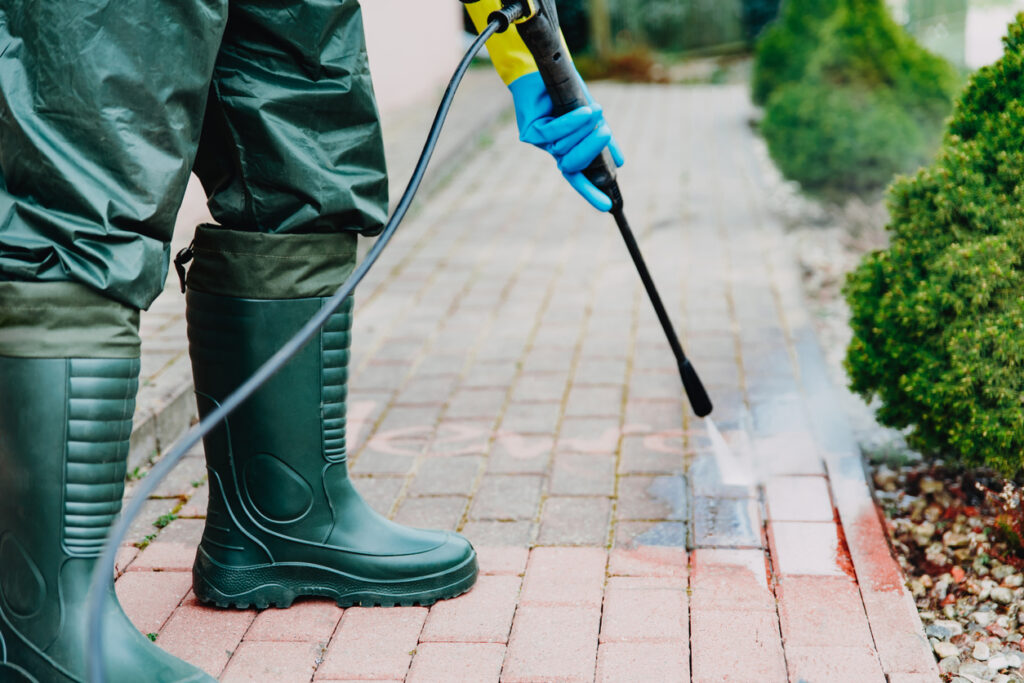 Man cleaning red, concrete pavement block using high pressure water cleaner