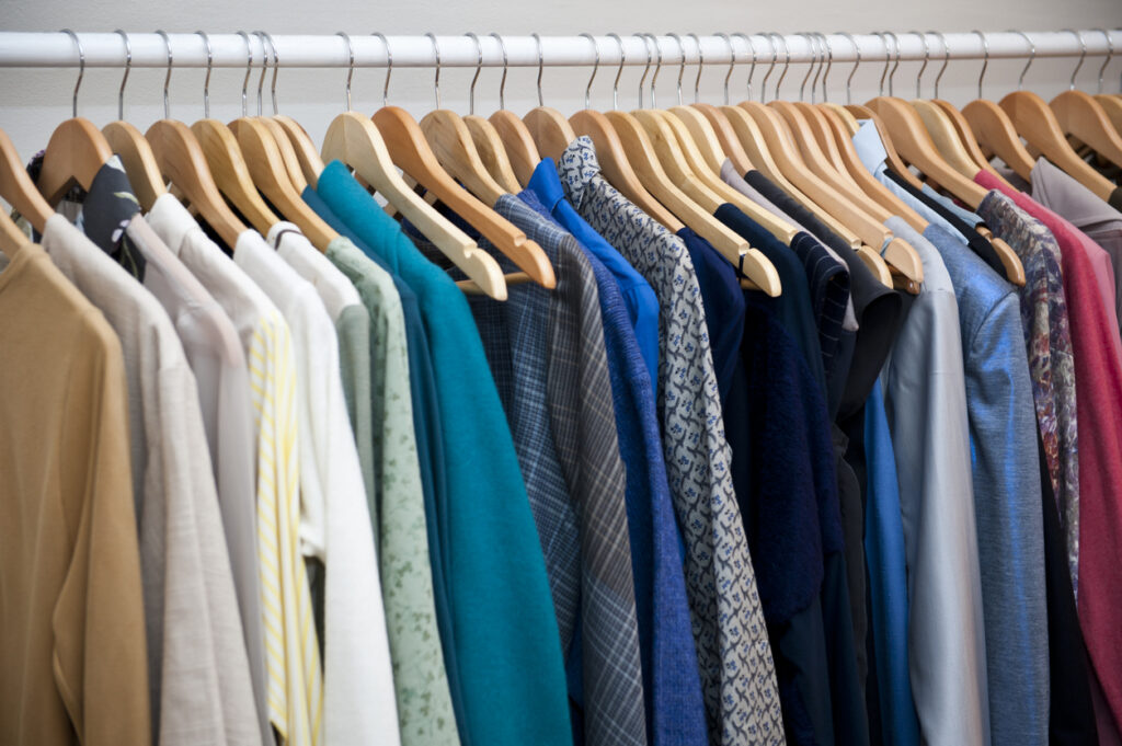 A white tension rod with multi-colored clothing hanging on it