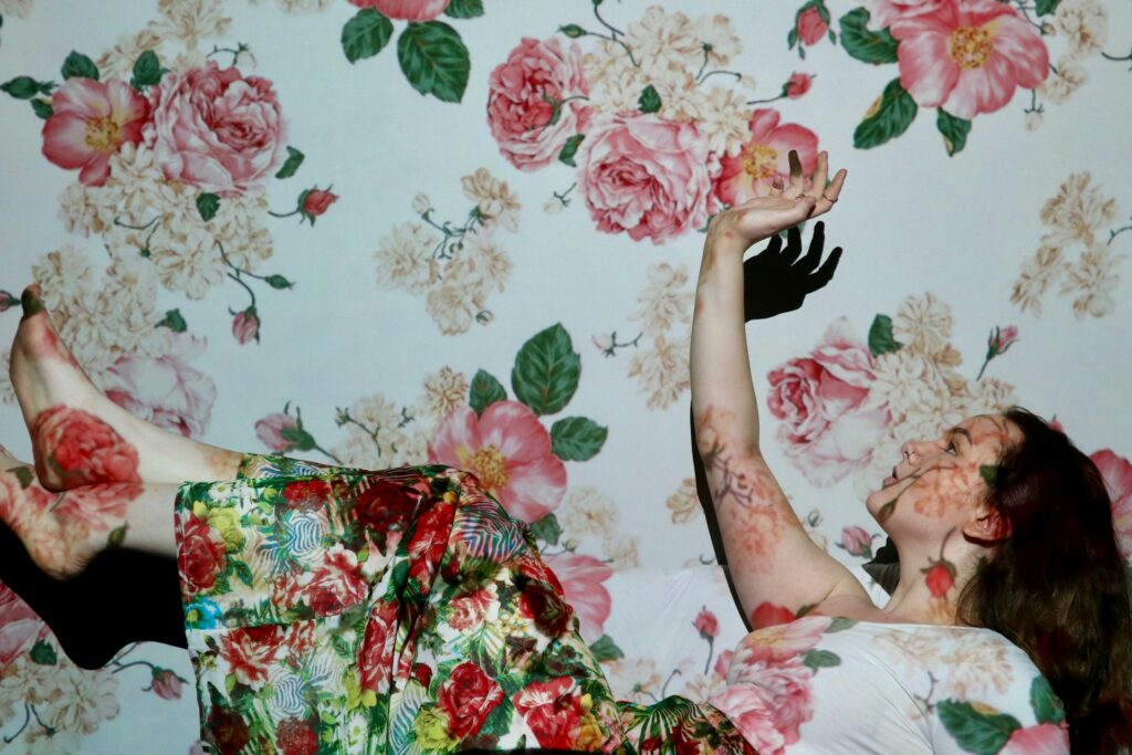 Woman with a flowery artistic design projected on her and wall behind her