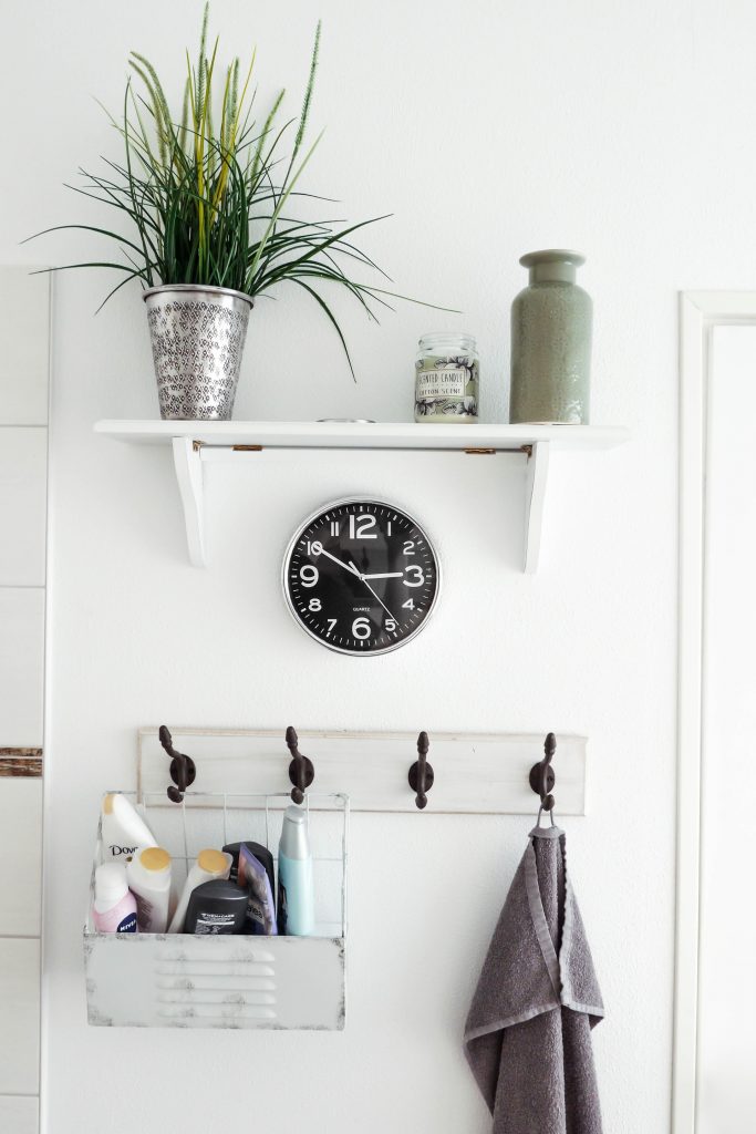 Four bathroom hooks under a clock and a shelf