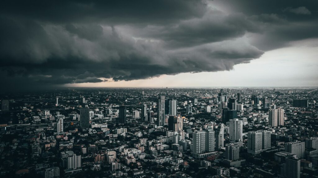 An expansive city with skyscrapers sits under a sky mostly filled with an oncoming thunderstorm system.