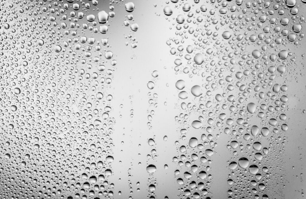 Water droplets sit on a glass pane against a gray-white background.