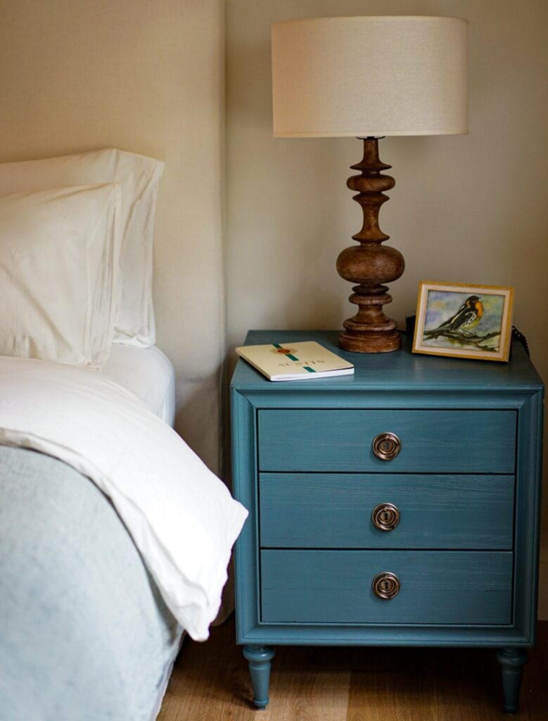 A teal nightstand with three drawers and a lamp and two books on it