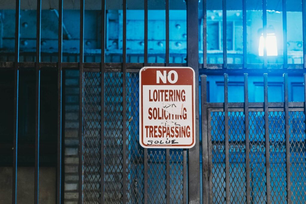 A No Loitering, Soliciting and Trespassing sign with graffiti mounted on a metal gate.