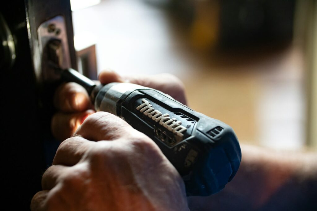 Man uses a black power drill on a door