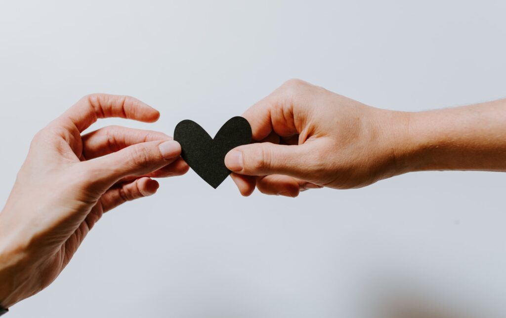 two hands holding a black paper cut-out heart