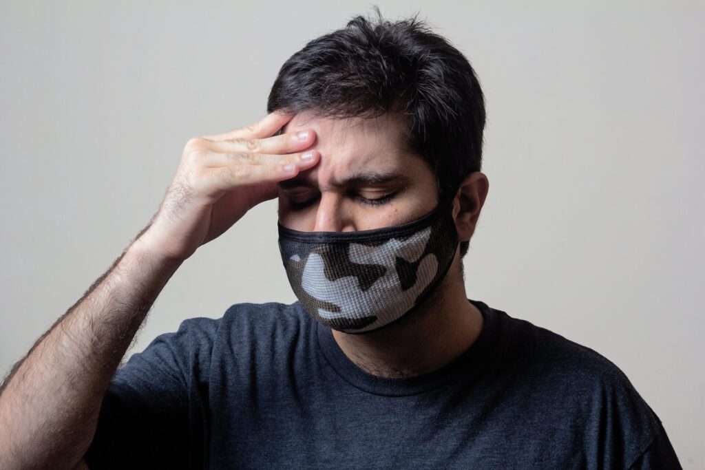 A mask-wearing man holding with aching head.