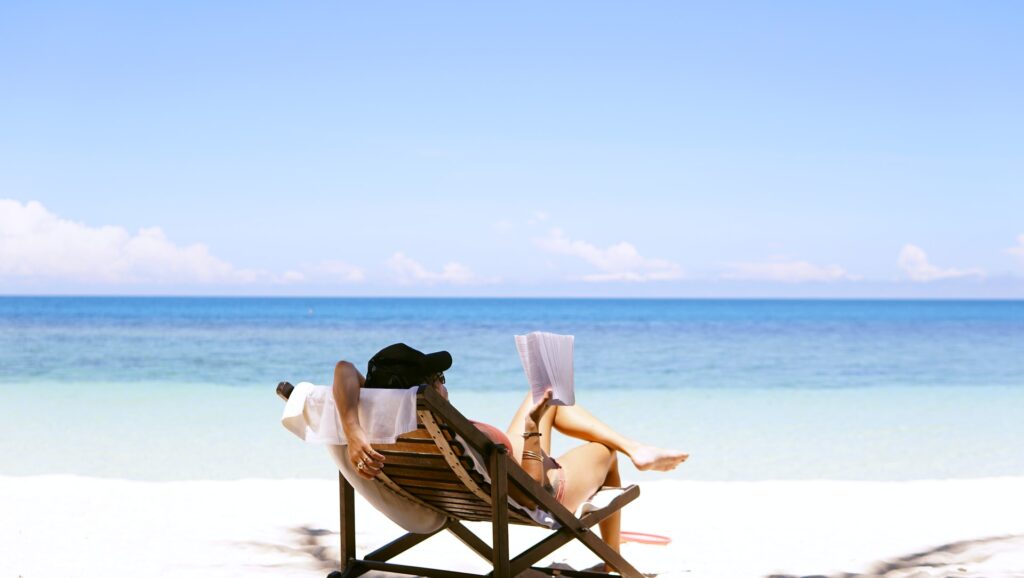 a woman wearing a pink bathing suit and black ballcap reading on a chair at the beach after decluttering