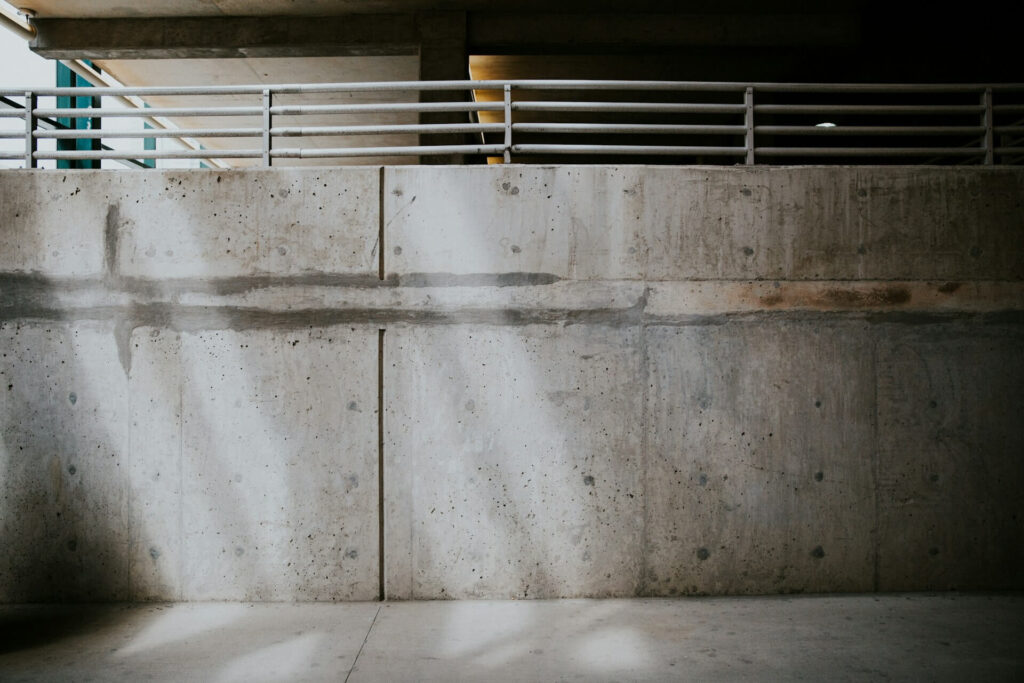 Gray concrete parking garage wall with a white metal rail, cast in light and shadow