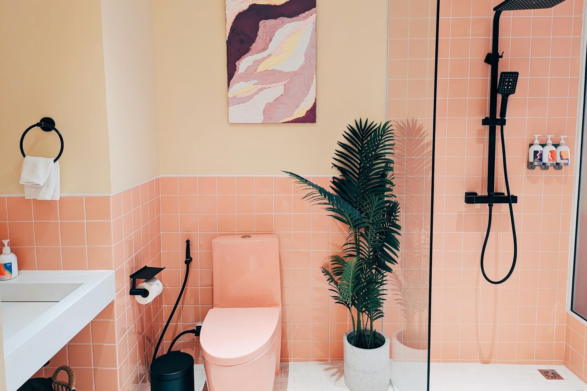 Bathroom with pink tiles, a toilet, and a corner plant