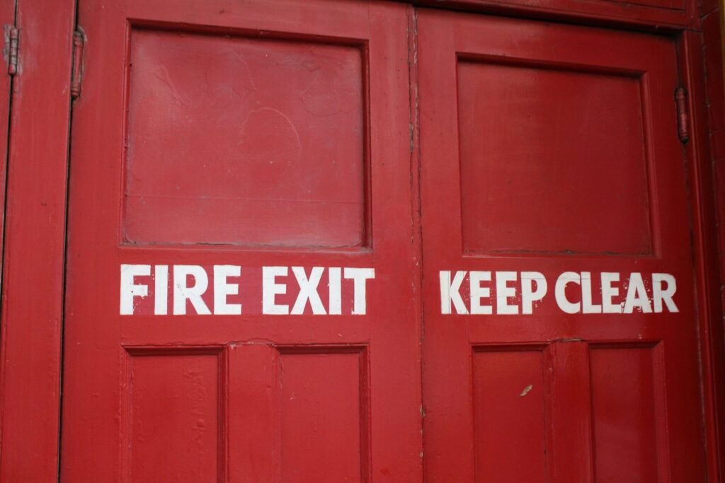 Red wooden fire door with two fire exit signs mounted on it