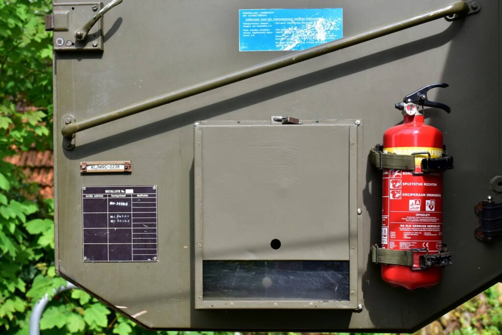 Red fire extinguisher mounted on a green metal panel