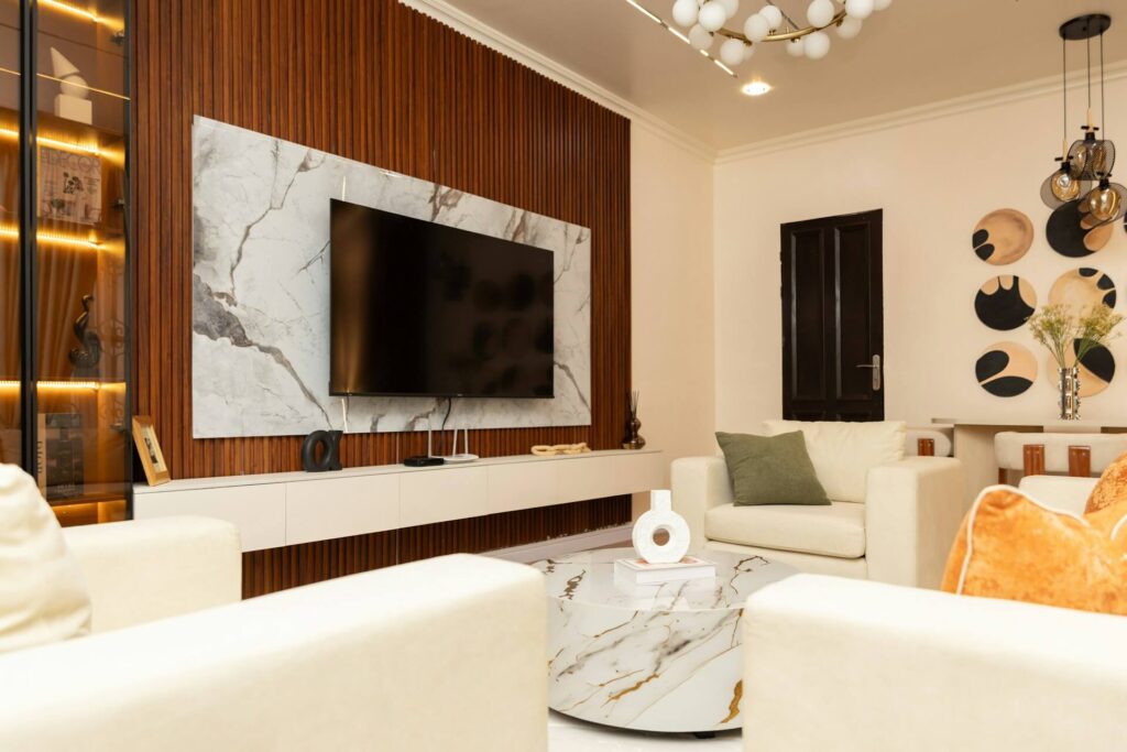 Modern living room with a wall-mounted TV, white sofas and marble accent wall