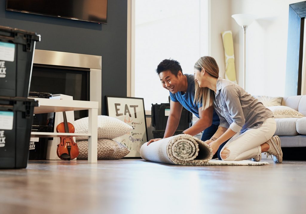 A man and a woman unrolling a carpet on their hardwood floors
