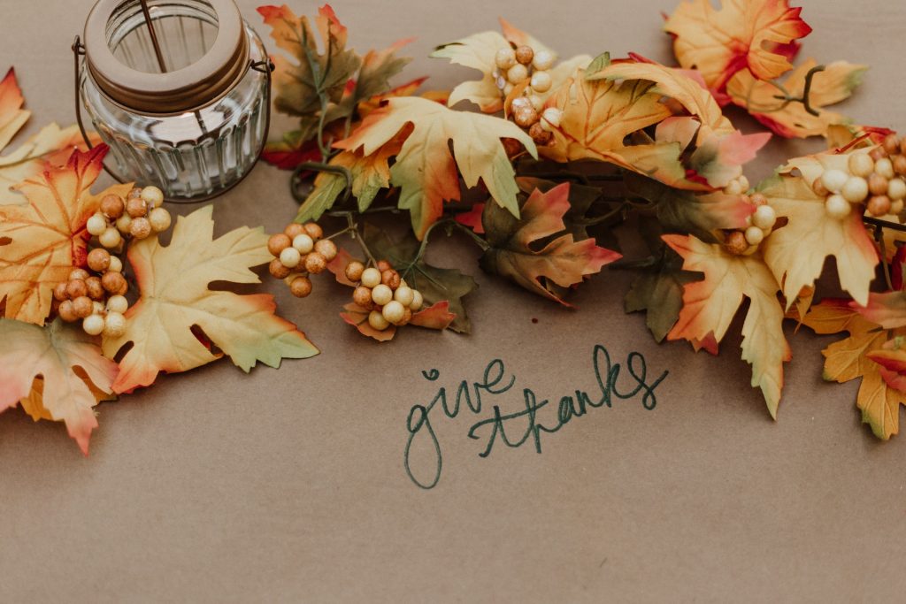 A faux fall garland and a candle on brown parchment paper with "give thanks" written on it