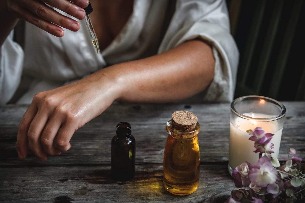 A woman in a white blouse using essential oils near a lit candle