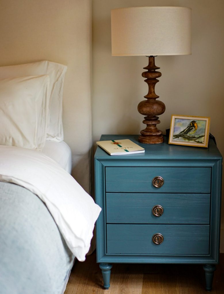 A teal nightstand with three drawers and a lamp and two books on it