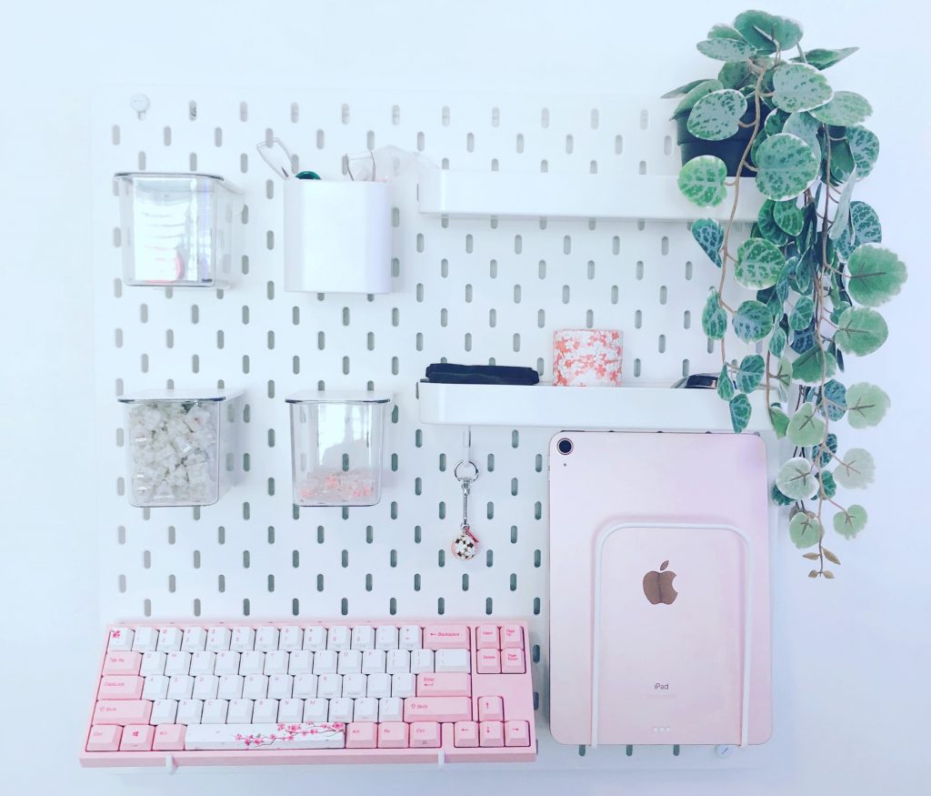 A white pegboard with white, pink, and green accessories hanging
