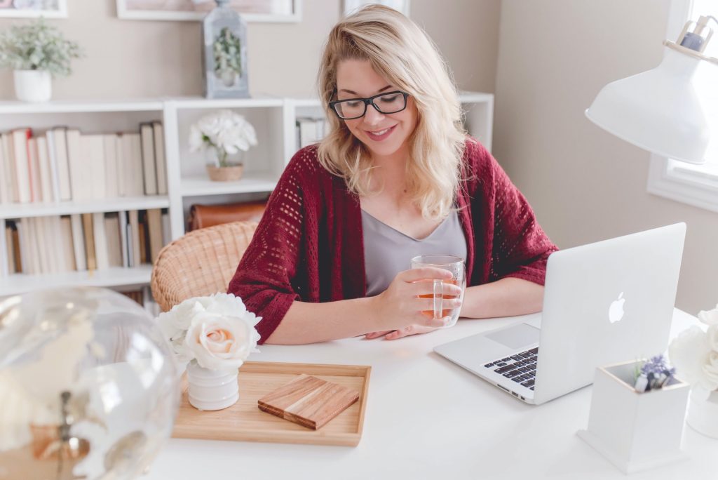 A woman with glasses sitting with tea and working on her laptop