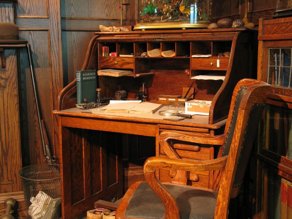 A cherry wood secretary desk cluttered with items