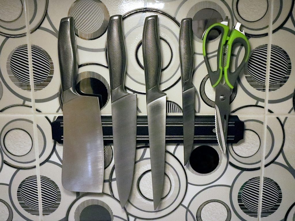 A set of knives and scissors hanging on a magnetic knife holder strip