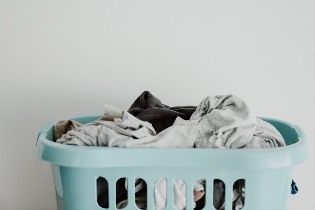 A teal laundry basket with neutral-colored clothes in it