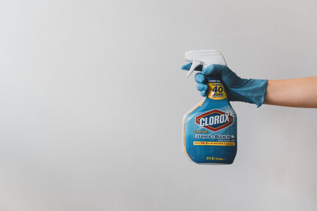 A person holding a spray bottle of bleach while wearing blue rubber gloves