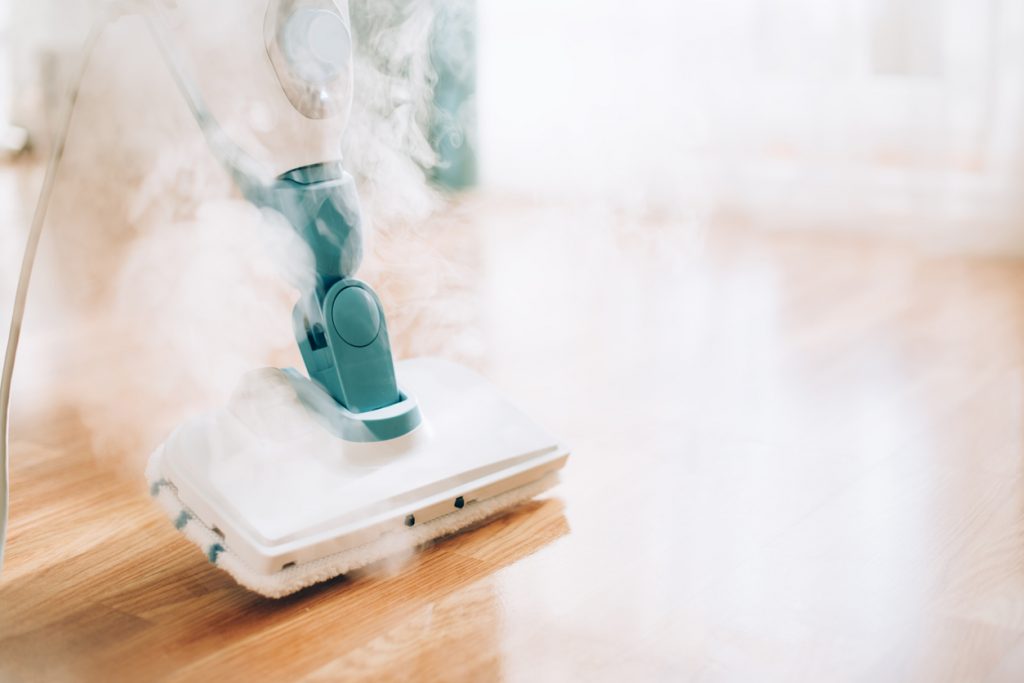Steam cleaner mop cleaning on a wooden floor as a cleaning supply essential