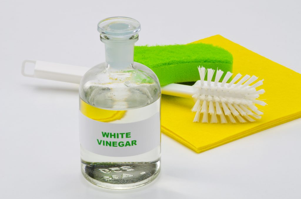 White vinegar in a glass jar with a green sponge, yellow rags, and a bottle brush